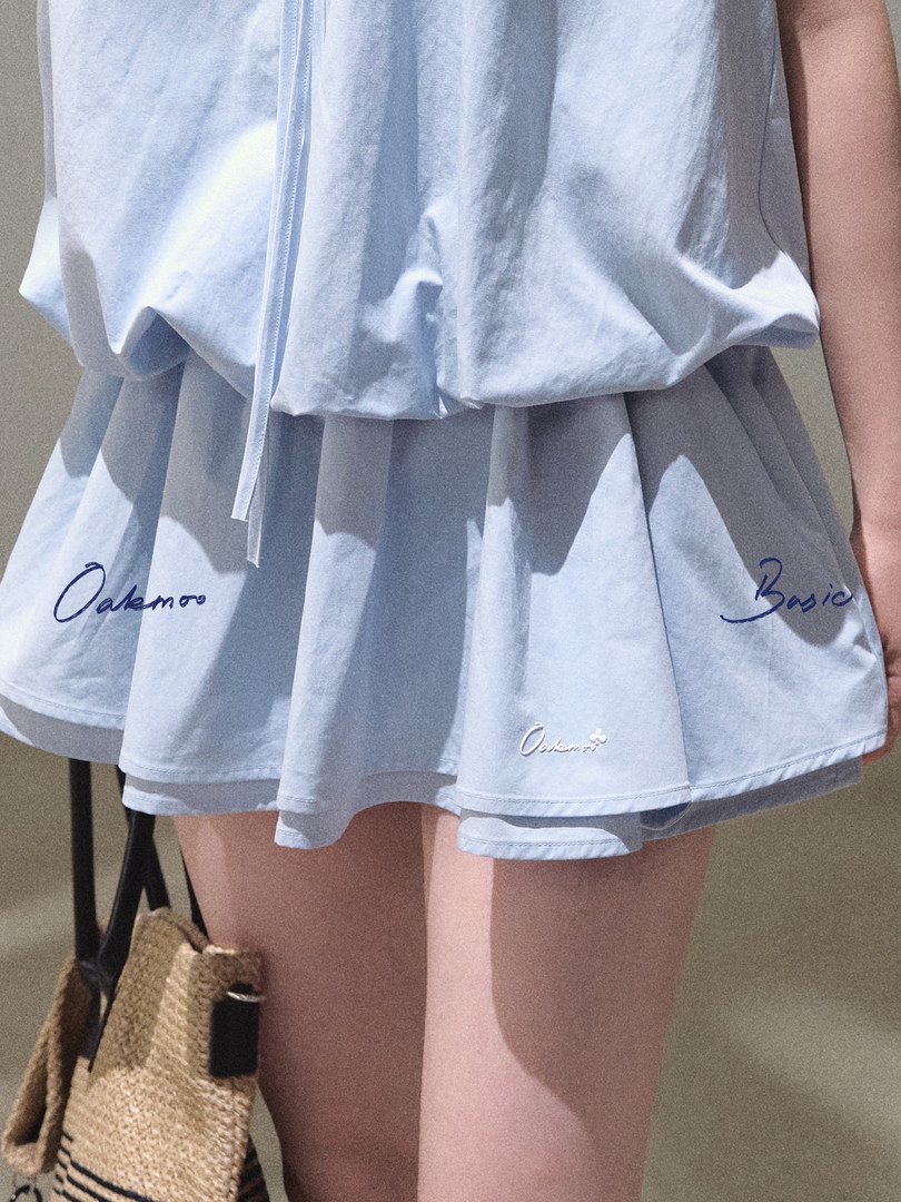 Light blue pleated skirt worn by a model with printed text detail