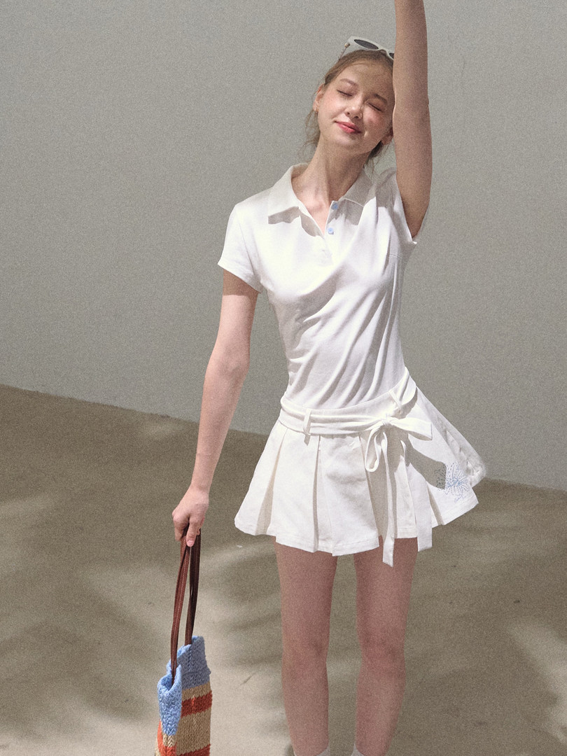 Woman wearing a white polo shirt and white pleated skirt with a tied waist