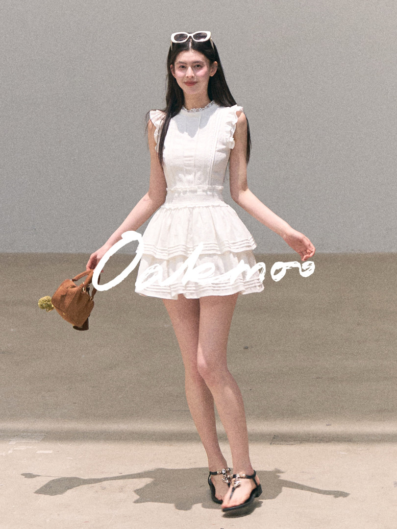 Model wearing a white ruffled sleeveless dress with black sandals and a brown handbag