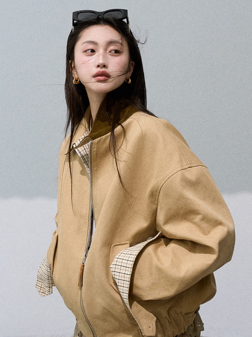 Model wearing a tan bomber jacket with plaid trim