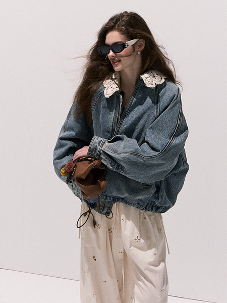 Model wearing an oversized denim jacket with lace collar, cream pants, and sunglasses