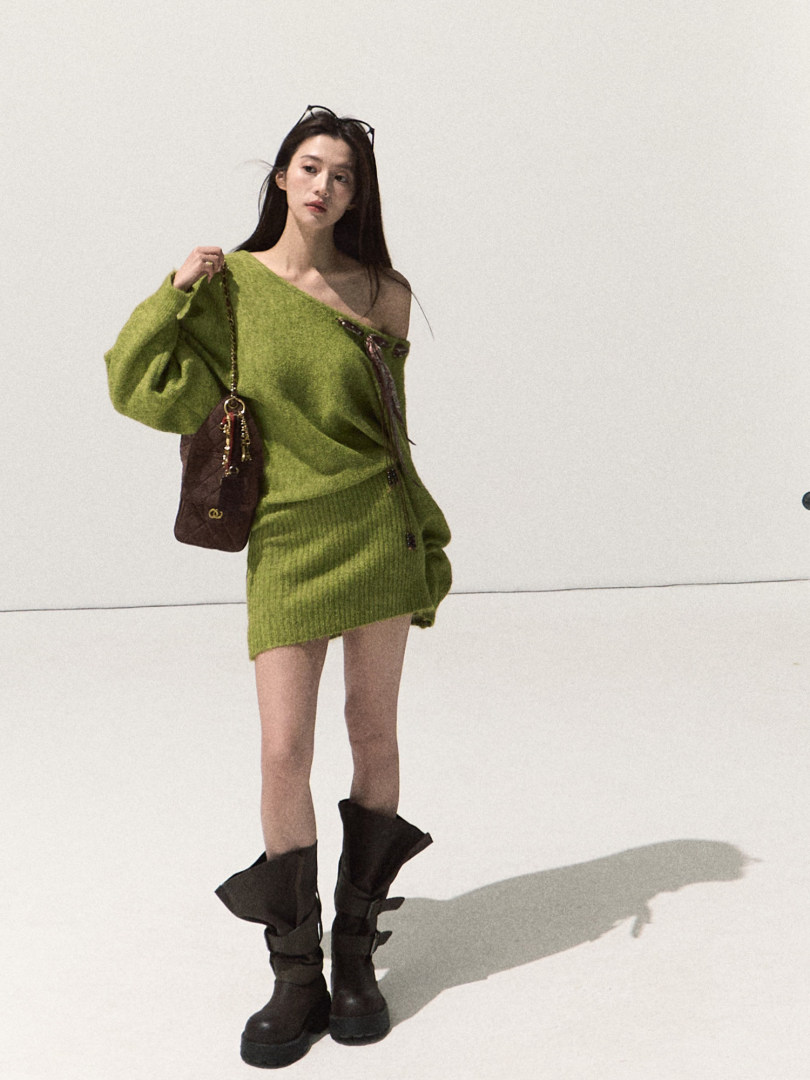 Model wearing a green off-shoulder knit mini dress with black boots and a brown shoulder bag