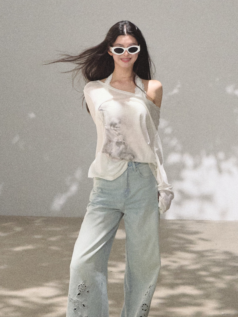 Model wearing a sheer white top, light blue jeans, and white sunglasses