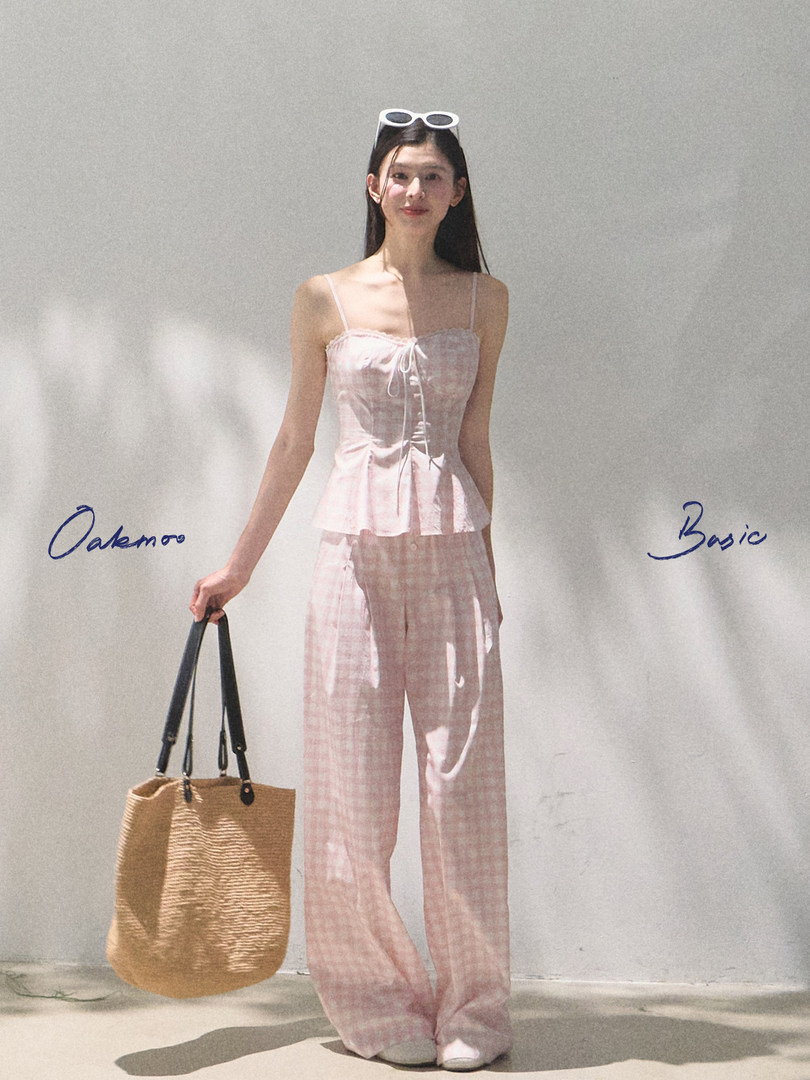 Model wearing a pink gingham camisole and wide-leg pants with a straw tote bag