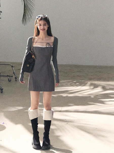 Woman wearing a gray long-sleeve mini dress with black boots and a black handbag