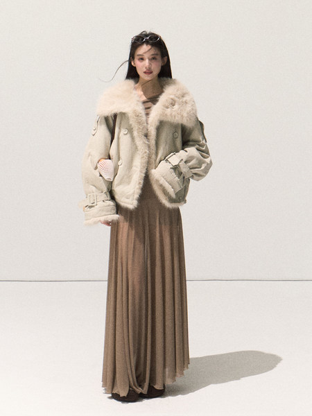 Model wearing a beige fur-trimmed coat over a long pleated dress