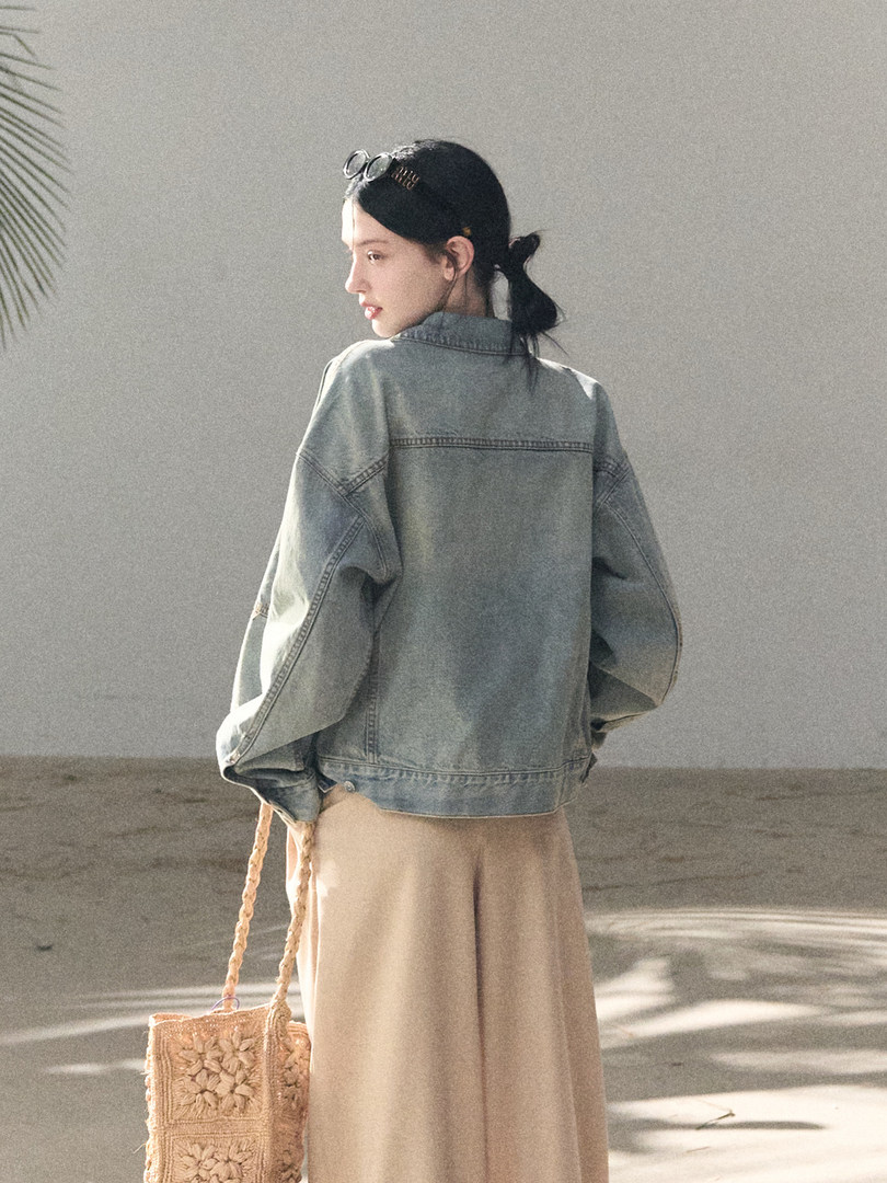 Model wearing an oversized light blue denim jacket with a woven straw tote bag