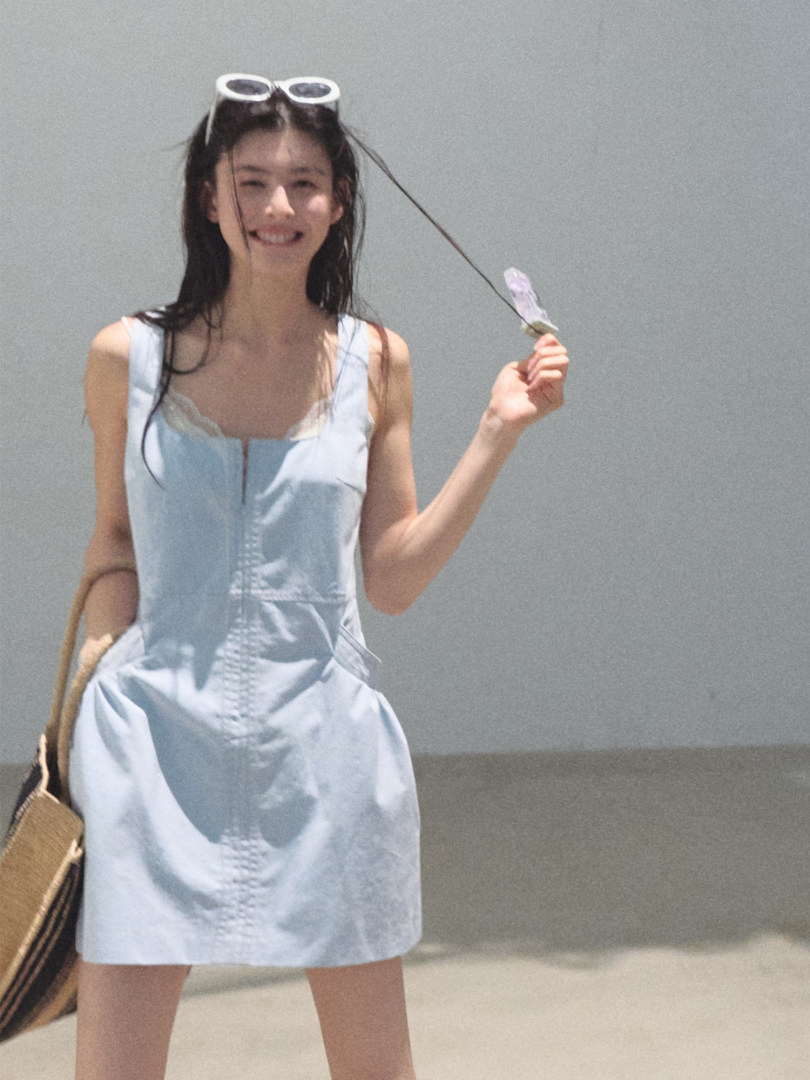 Woman wearing a light blue sleeveless dress with a small handbag