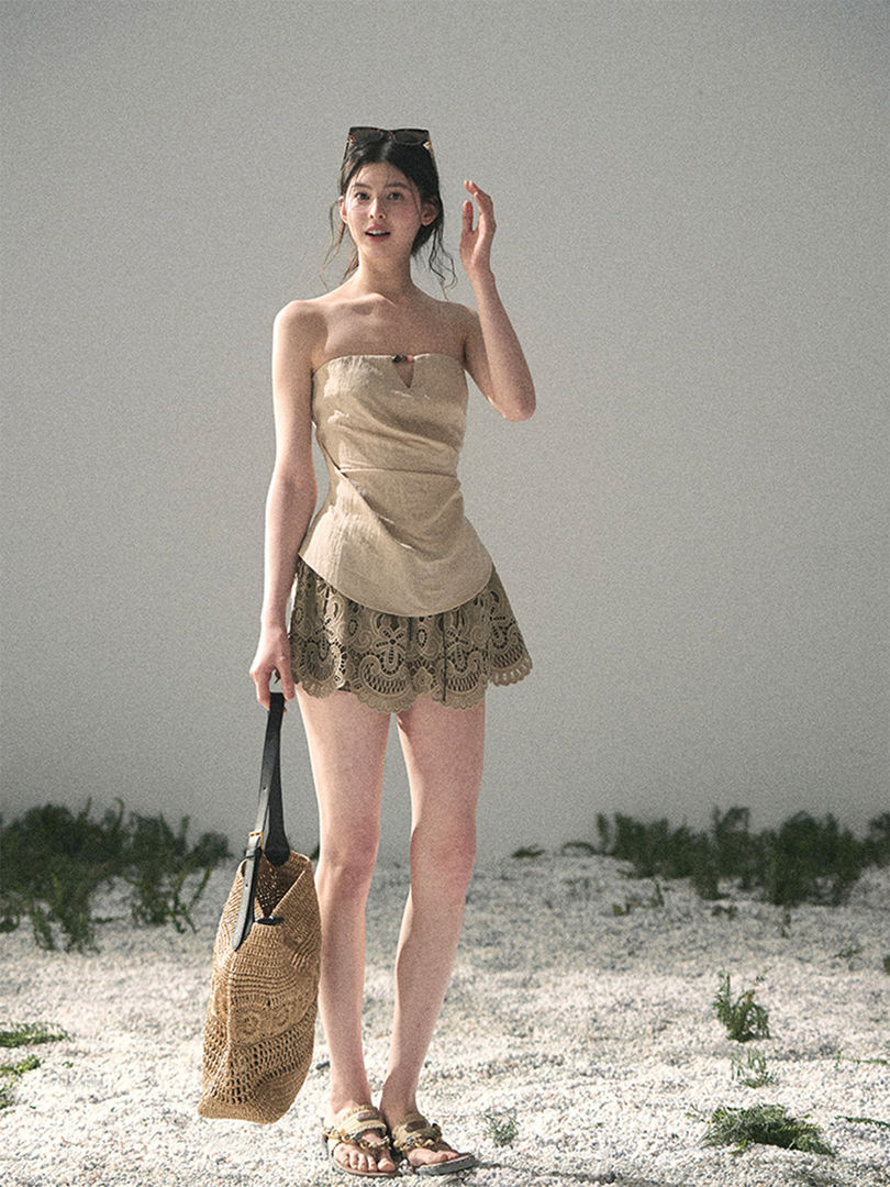 Woman wearing a beige strapless top and lace shorts with a woven tote bag at the beach