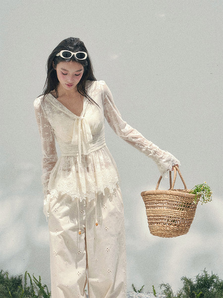 Model wearing a cream lace dress and holding a woven straw tote bag
