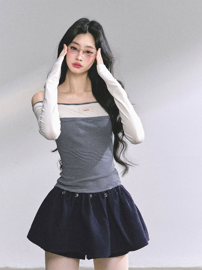 Female model wearing a striped sleeveless top with white arm sleeves and a dark mini skirt