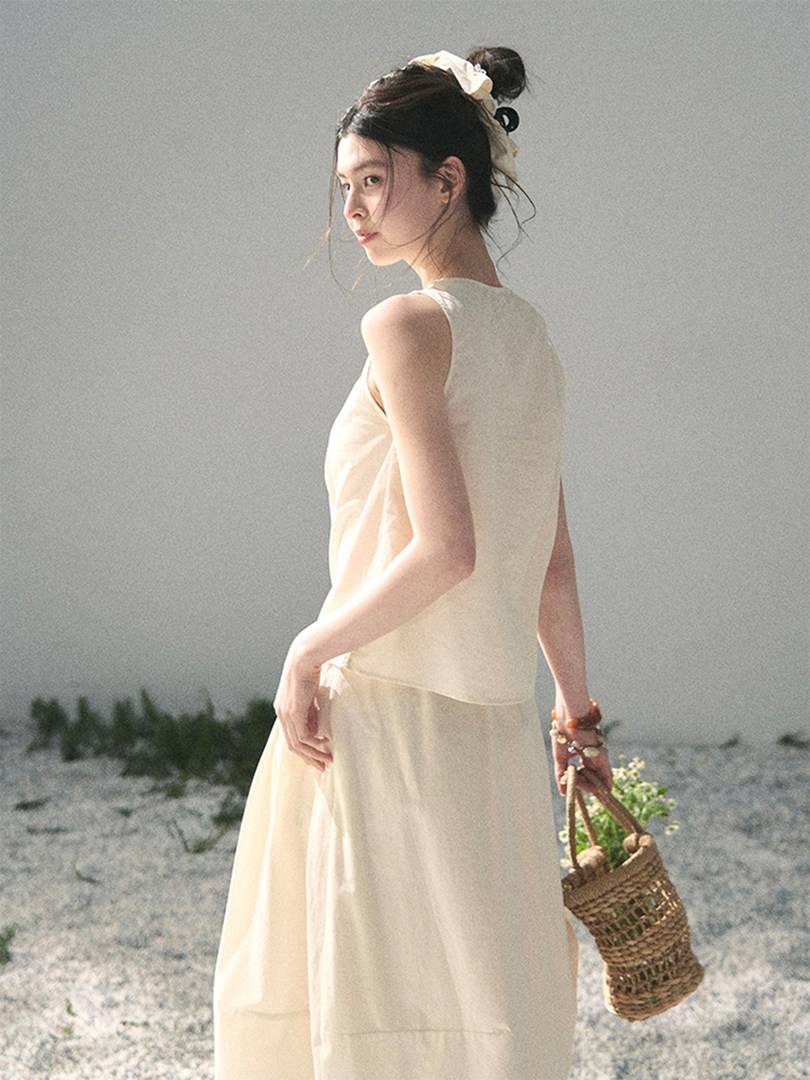 Woman wearing a cream sleeveless dress and holding a woven bag outdoors