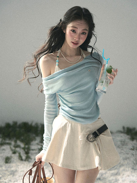 Woman wearing a light blue off-shoulder top with a cream mini skirt on a beach.