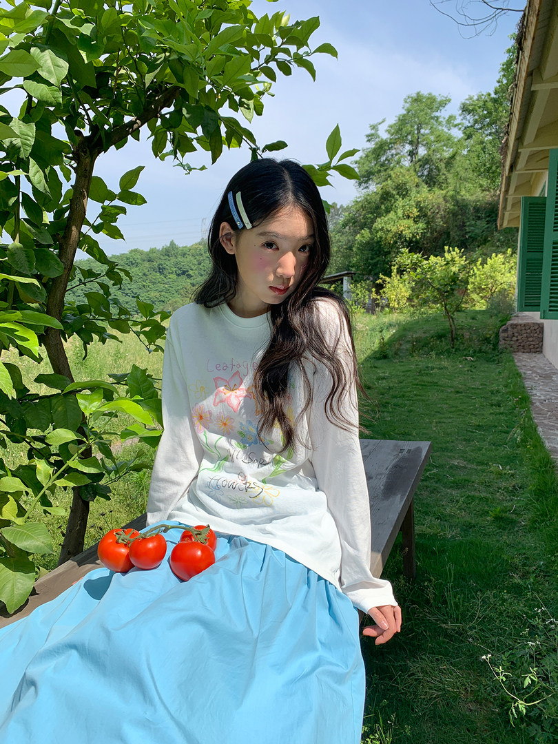 Young woman wearing a white graphic long-sleeve top and blue skirt outdoors