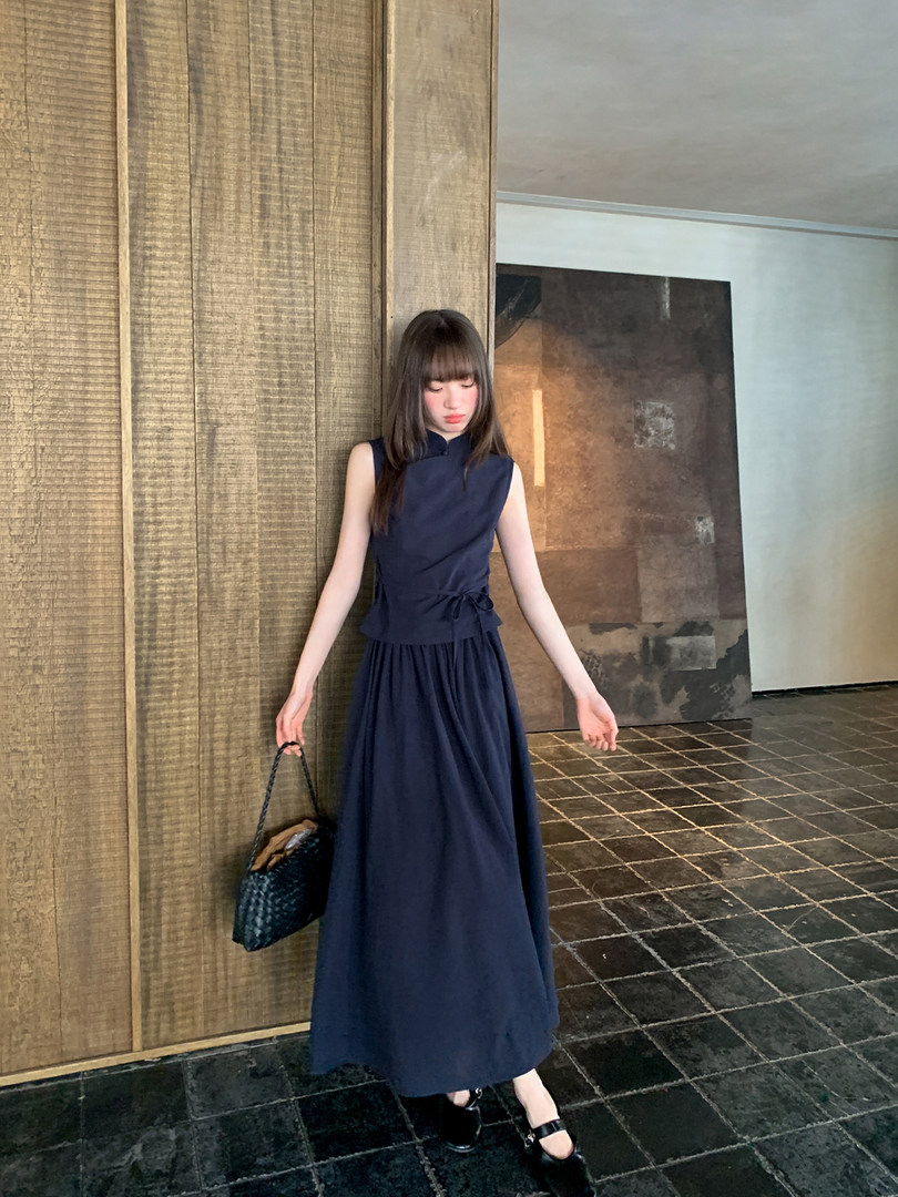 Model wearing a navy sleeveless long dress with a cinched waist and pleated skirt