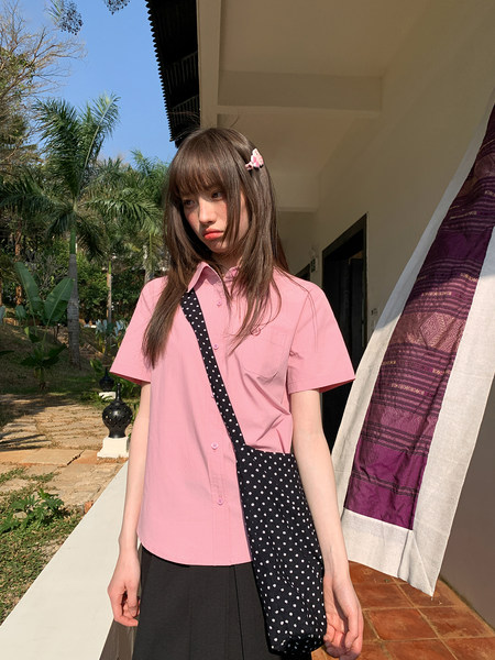 Model wearing a pink short-sleeve button-up shirt with a black polka-dot shoulder bag outdoors