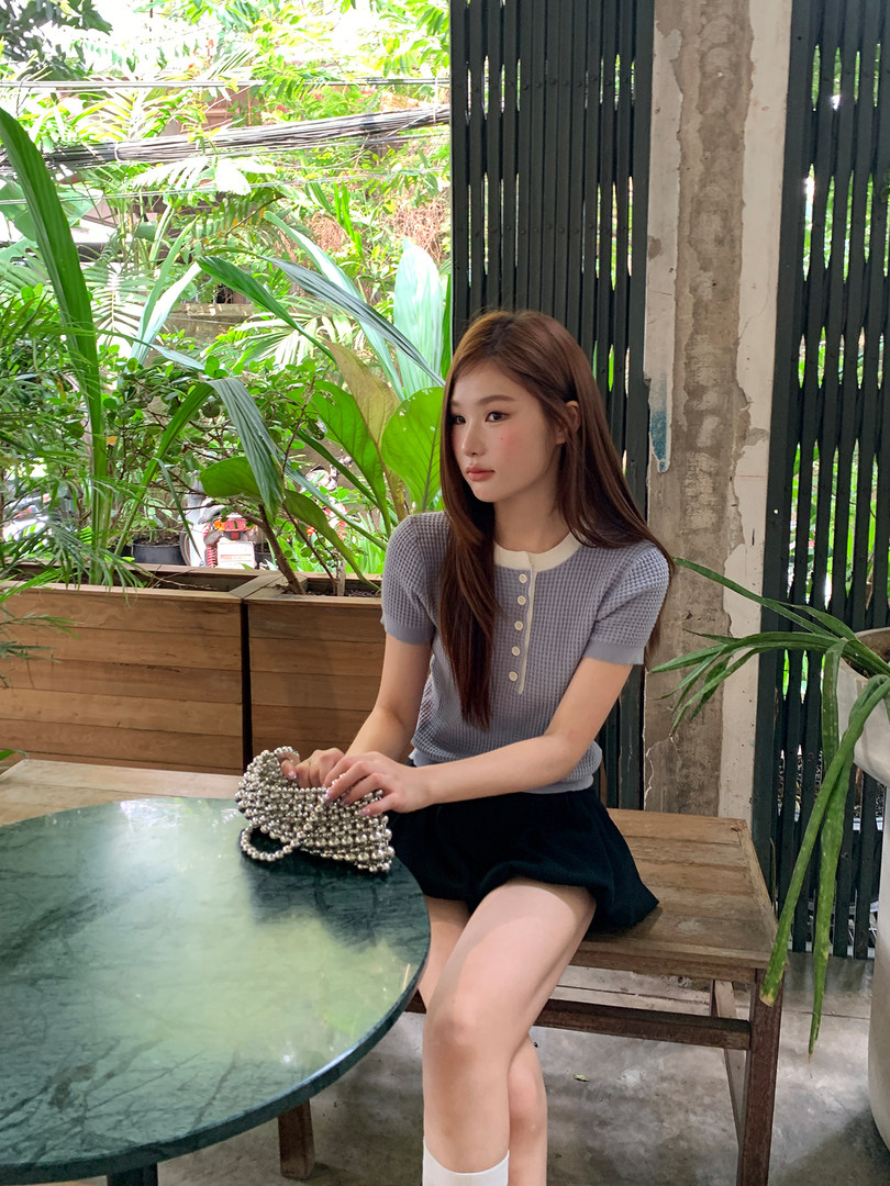 Model wearing a light blue short-sleeve knit top and black skirt while holding a beaded handbag