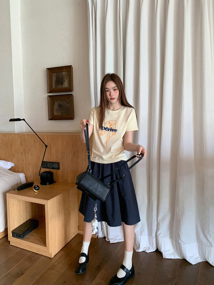 Woman wearing a cream graphic T-shirt, navy skirt, and black crossbody bag
