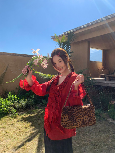 Woman wearing a red ruffled blouse with a leopard print handbag outdoors