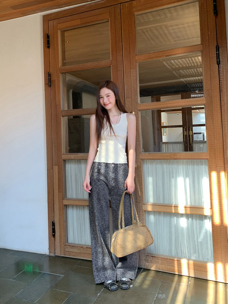 Woman wearing a white sleeveless top with gray patterned wide-leg pants and a tan handbag
