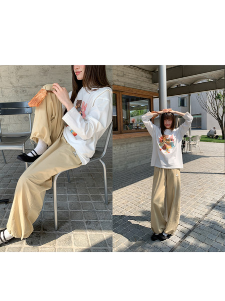 Model wearing a white graphic long-sleeve top and beige wide-leg pants outdoors