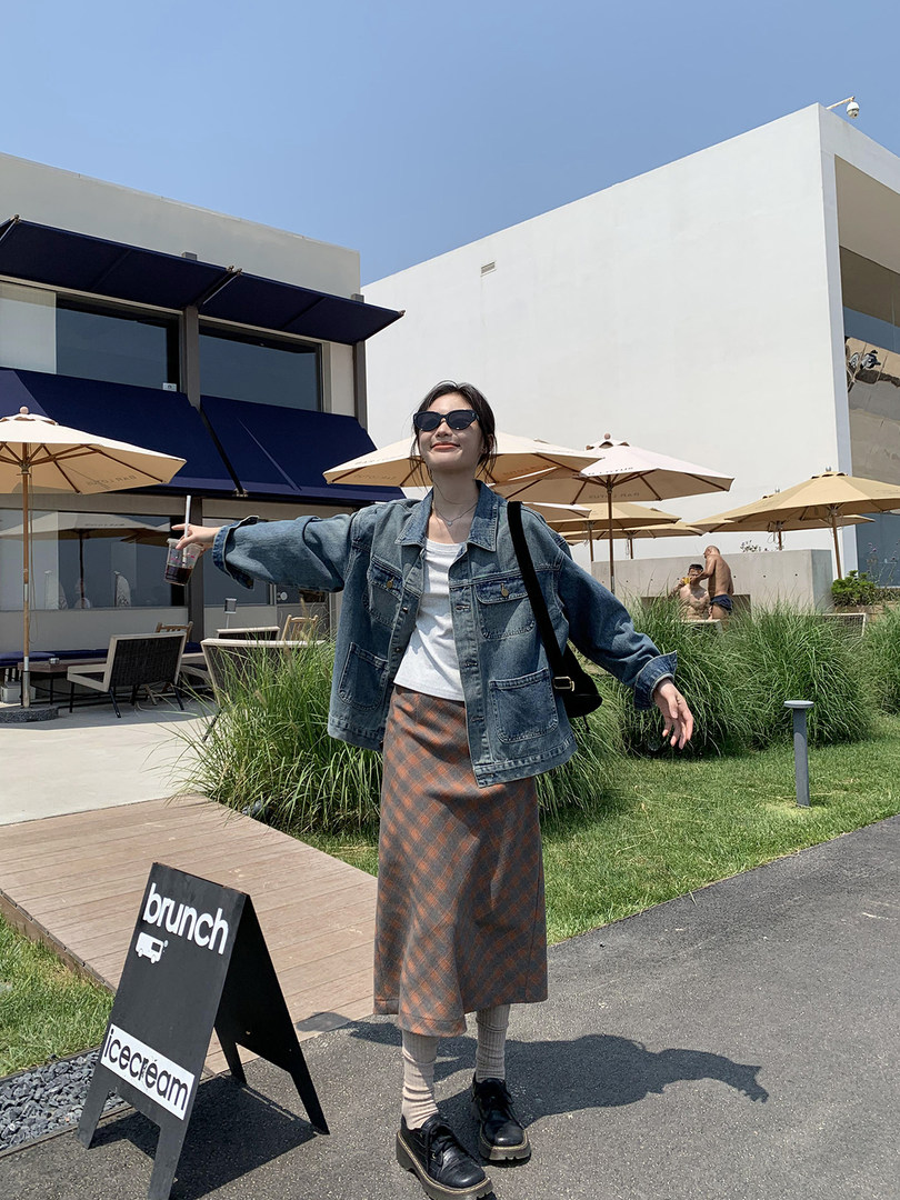 Woman wearing a denim jacket, white top, plaid skirt, and sneakers outdoors