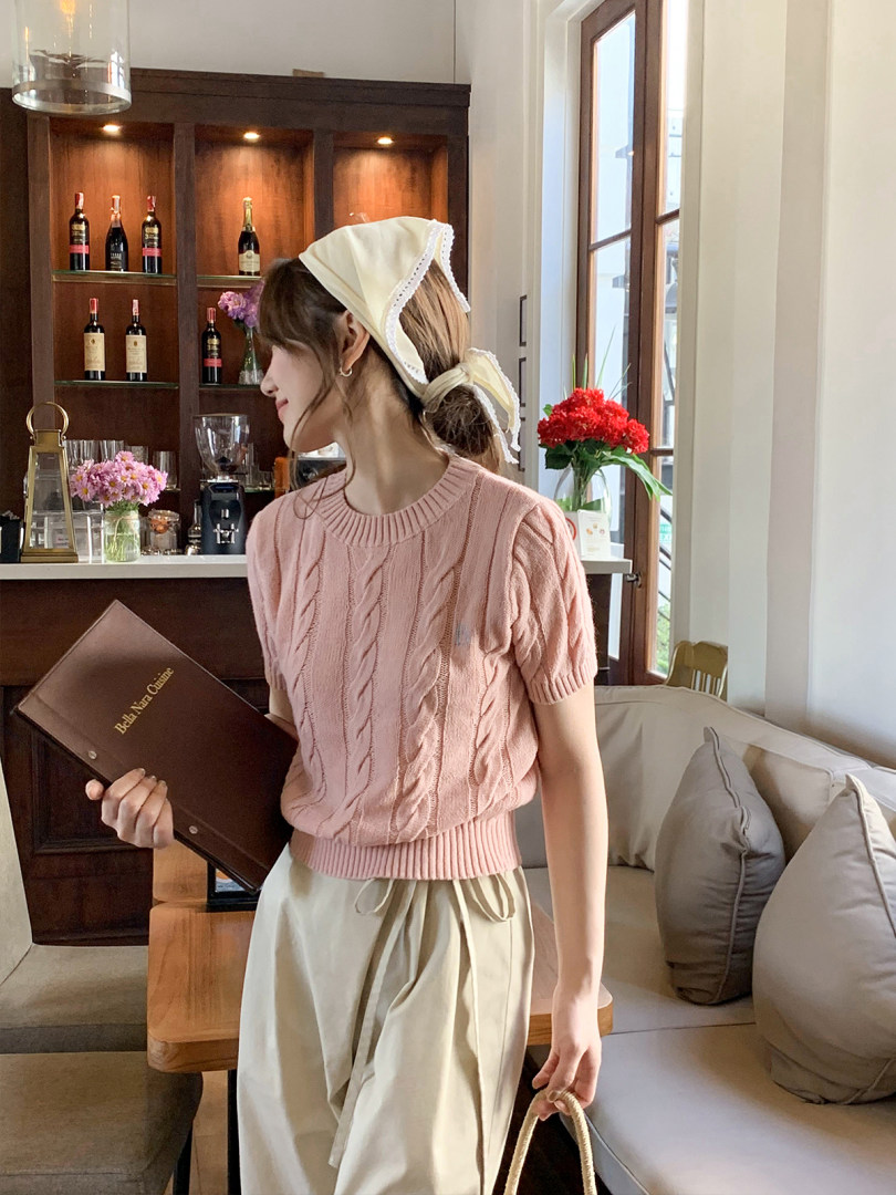 Woman wearing a pink cable-knit short-sleeve sweater with a cream skirt in a cafe setting