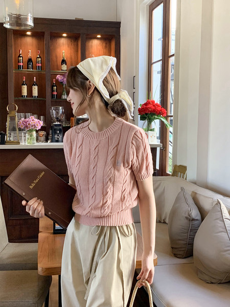 Woman wearing a pink cable-knit short-sleeve sweater with a cream skirt in a cafe setting