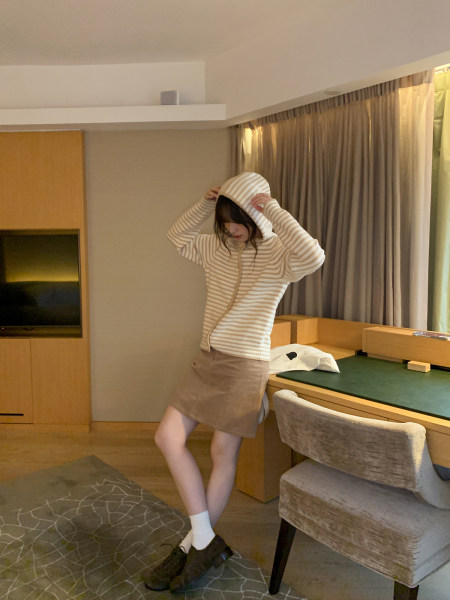 Woman wearing a striped hooded sweatshirt with a beige skirt indoors