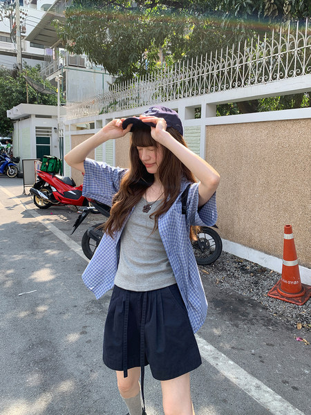 Young woman wearing a blue plaid overshirt, gray tank top, and black shorts outdoors