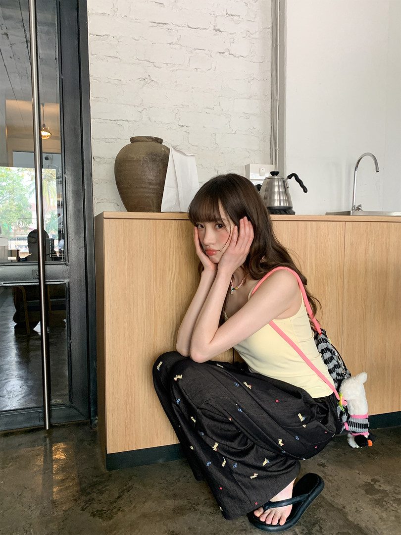Woman modeling a light yellow sleeveless top with a black patterned skirt and pink strap bag