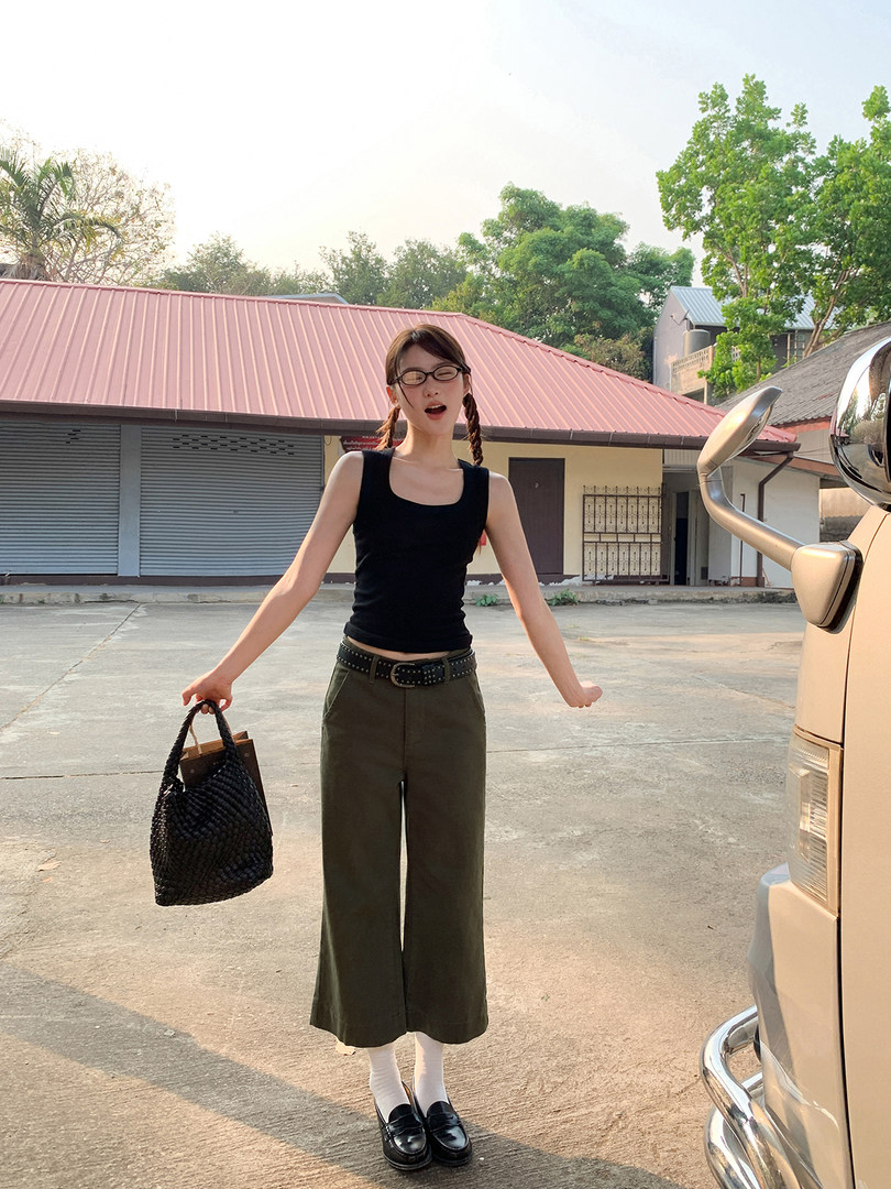 Woman wearing a black sleeveless top with wide-leg olive pants and a black woven handbag outdoors