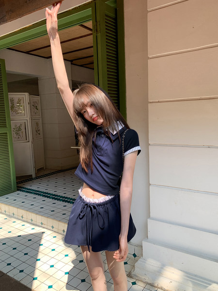 Model wearing a navy two-piece crop polo top and matching skirt set outdoors