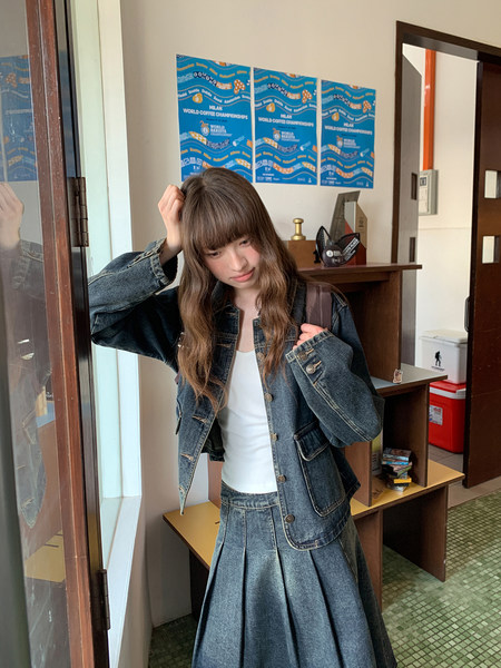 Woman wearing a denim jacket and pleated denim skirt over a white top