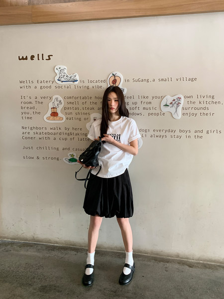 Model wearing a white graphic T-shirt, black skirt, and black Mary Jane shoes with a handbag