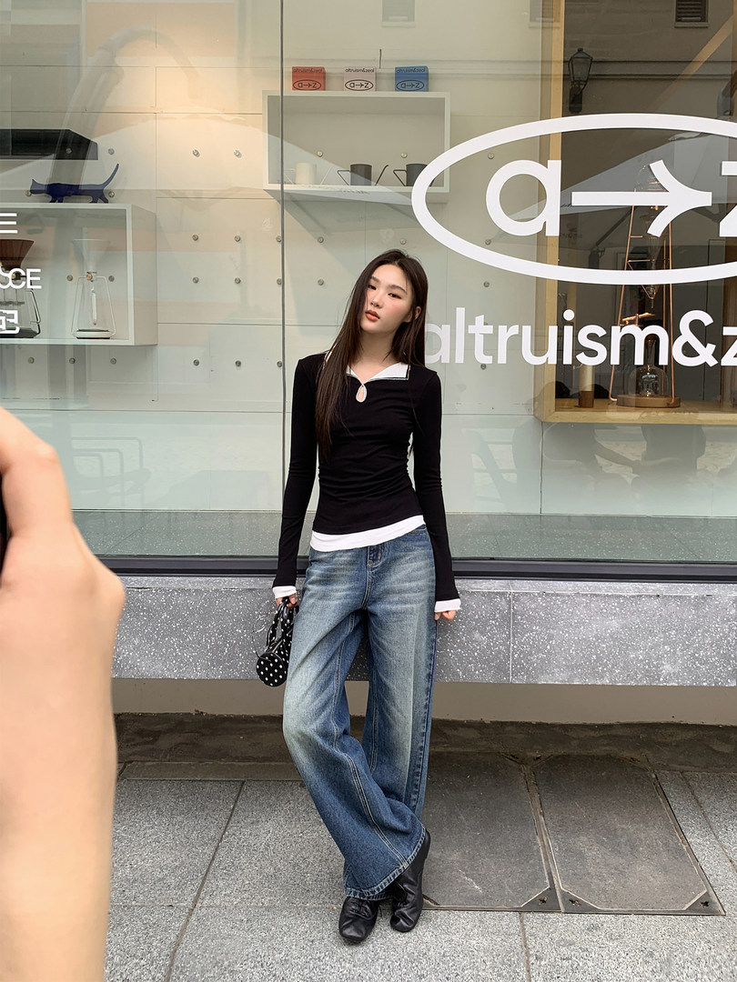 Full-body photo of a woman wearing a black long-sleeve top and loose blue jeans