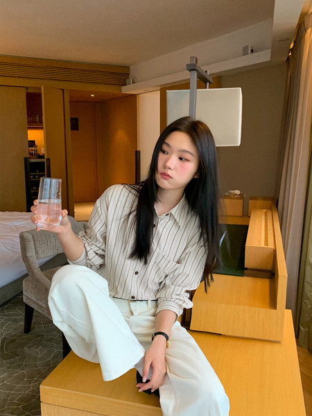 Woman wearing a striped button-up shirt and white pants while seated indoors
