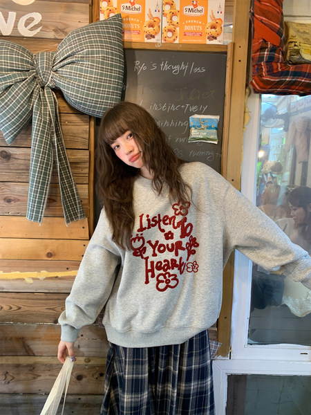 Model wearing a gray graphic sweatshirt with a plaid skirt in a cozy indoor setting