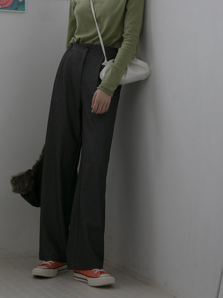 Model wearing dark wide-leg pants with a green top and white shoulder bag