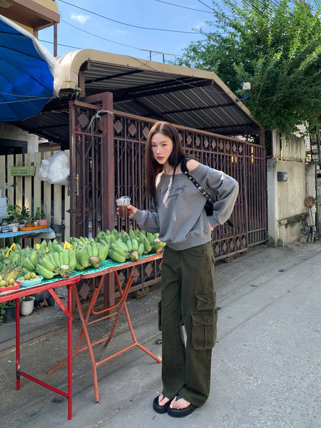 Woman wearing a gray off-shoulder sweatshirt and olive cargo pants outdoors