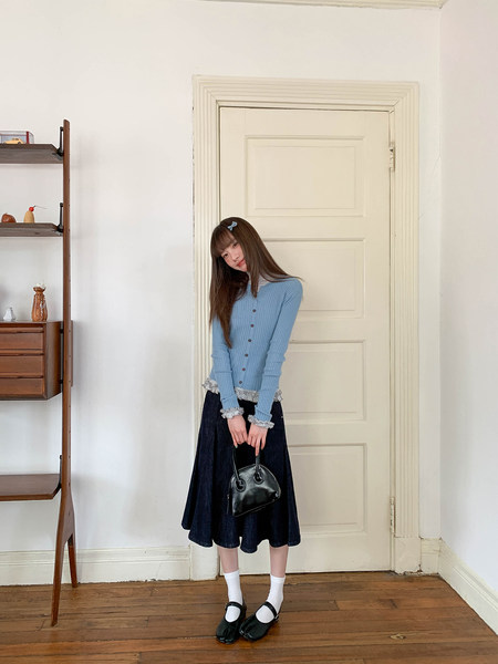 Young woman wearing a light blue ribbed top, dark skirt, and black Mary Jane shoes while holding a black handbag