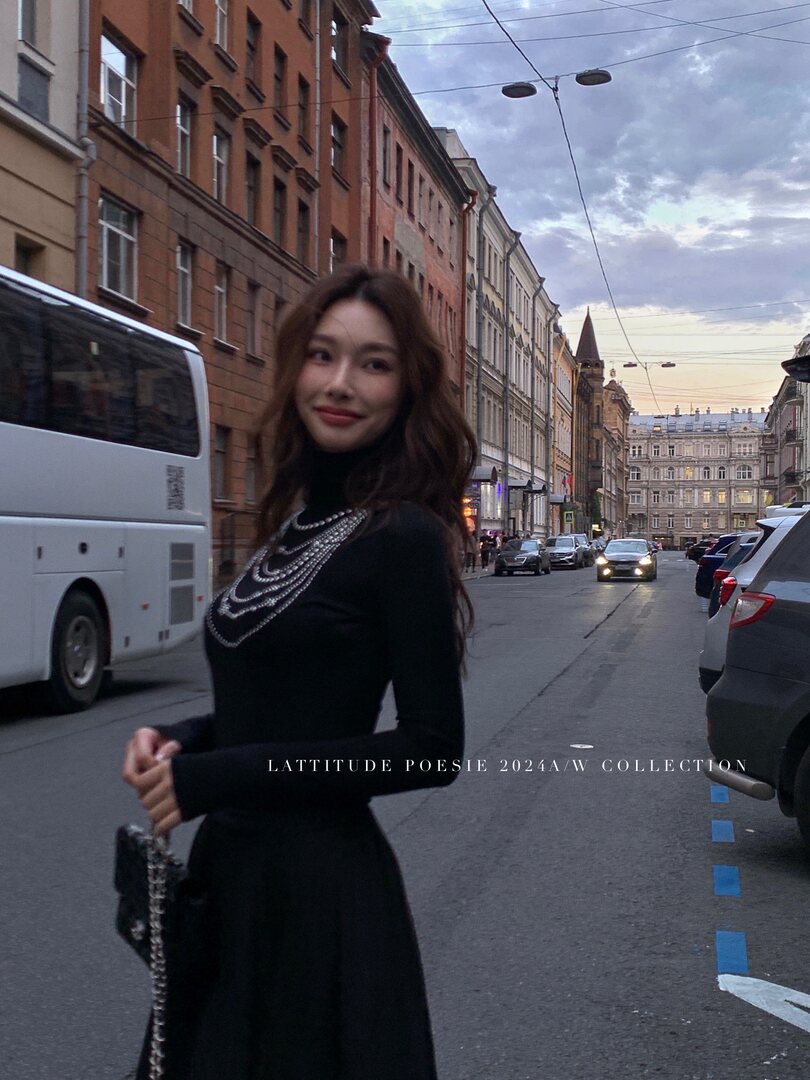 Model wearing a black long-sleeve dress and layered pearl necklace on a city street