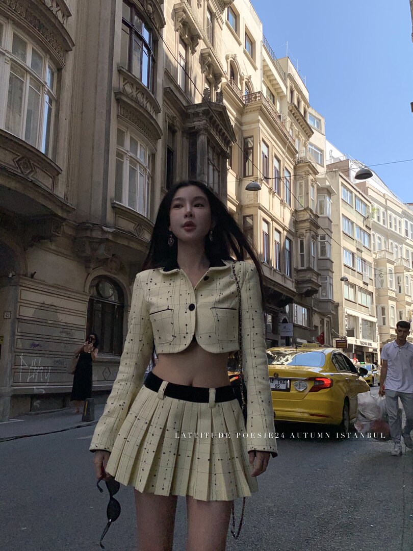 Model wearing a cream plaid cropped jacket and pleated mini skirt on a city street