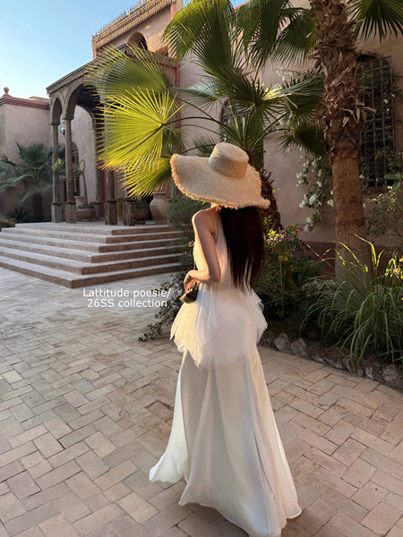 Woman wearing a flowing white dress and wide-brim straw hat in a tropical courtyard
