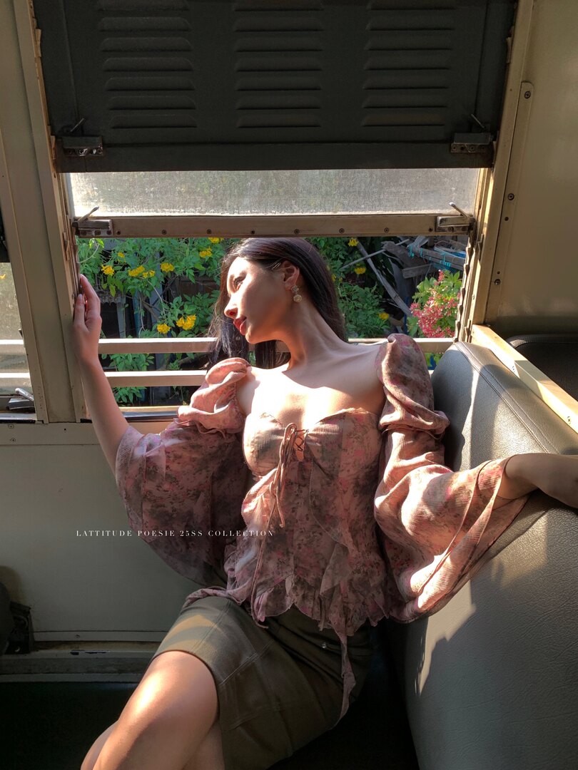 Model wearing a pink floral off-shoulder puff-sleeve blouse with lace-up front