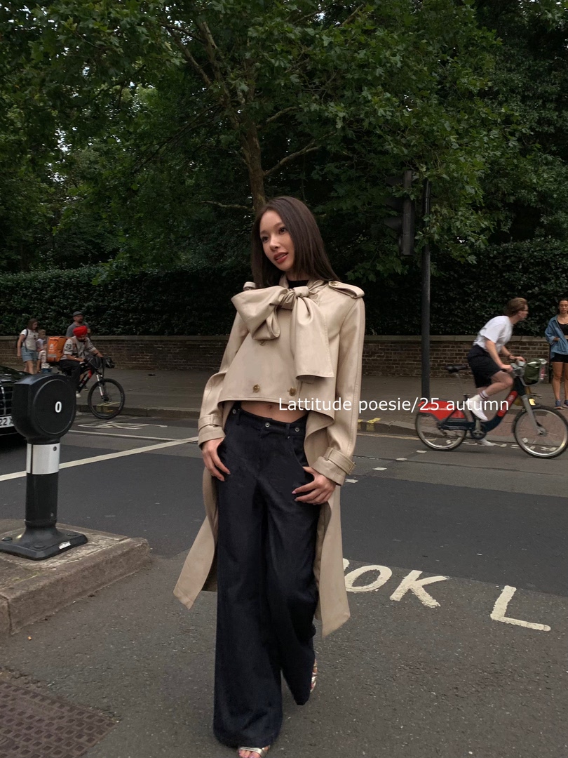 Woman wearing a beige trench coat with a large bow and black wide-leg pants outdoors