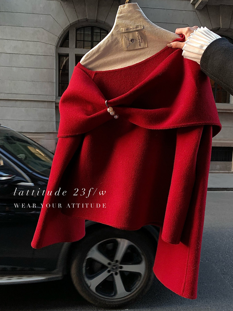 Red draped off-shoulder knit poncho or sweater held on a hanger outdoors