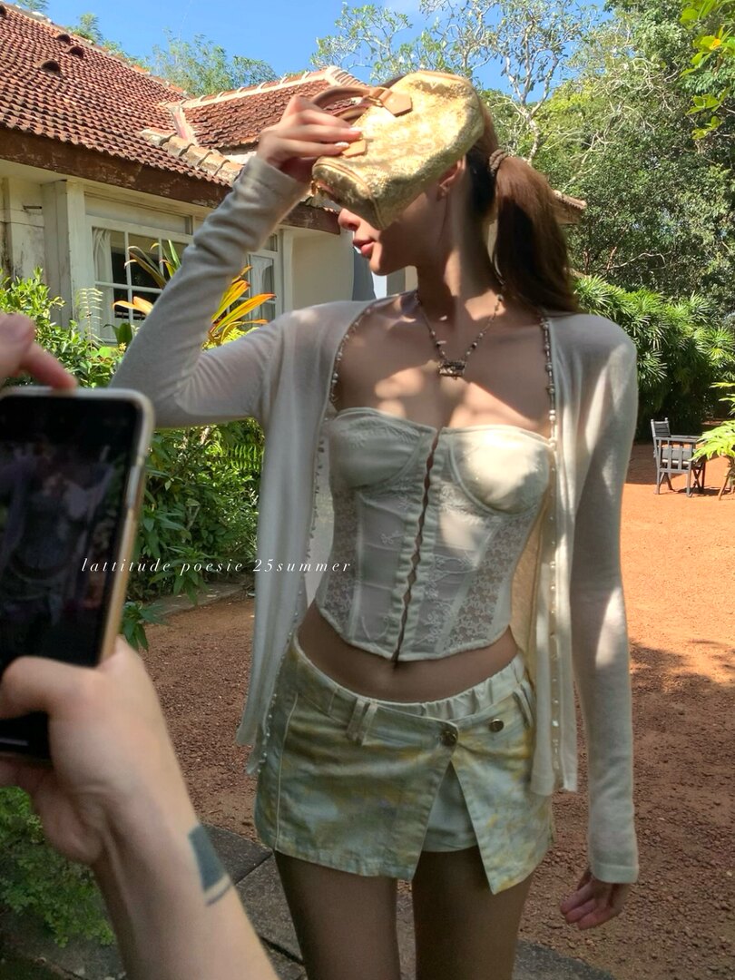 Woman modeling a light cream corset top, cardigan, and skirt outdoors