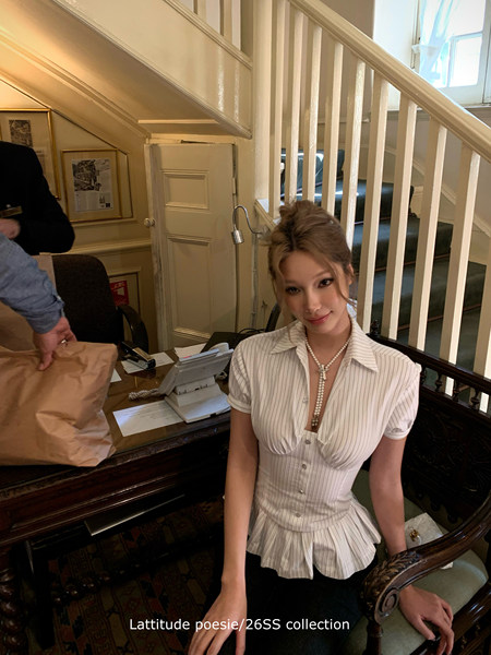 Model wearing a white striped short-sleeve button-up blouse with a peplum waist