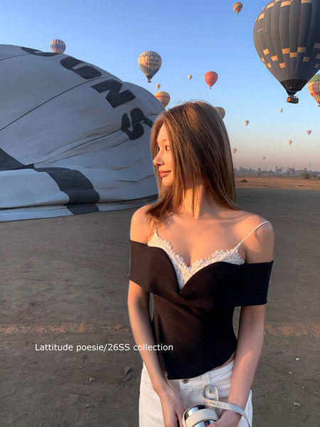Model wearing a black off-shoulder top layered over a white lace camisole outdoors
